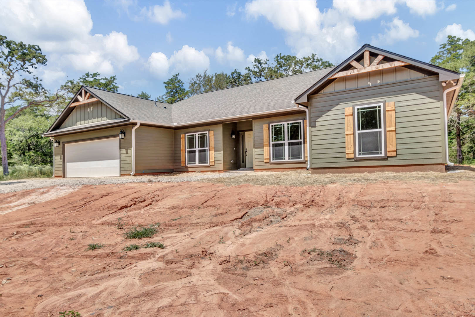 White-framed window set in a white wall, brown trim accents, house situated on dirt hill with trees and cloudy sky in background