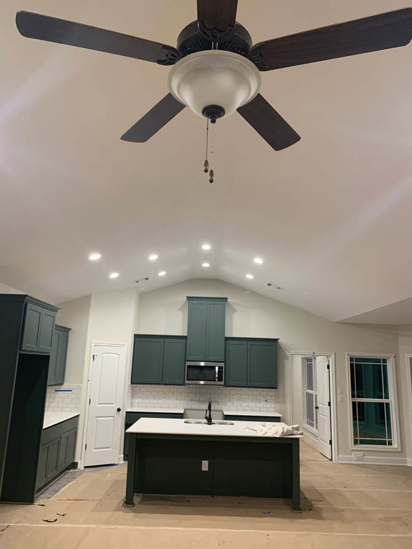 Ceiling fan with integrated light fixture above kitchen featuring white cabinetry, stone countertop with sink, close-up window, and white door with black knob
