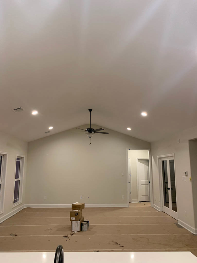 Ceiling fan with light fixture mounted on white plaster ceiling above boxes and cans scattered on hardwood floor, white door with black knobs and close-up detail, window with white