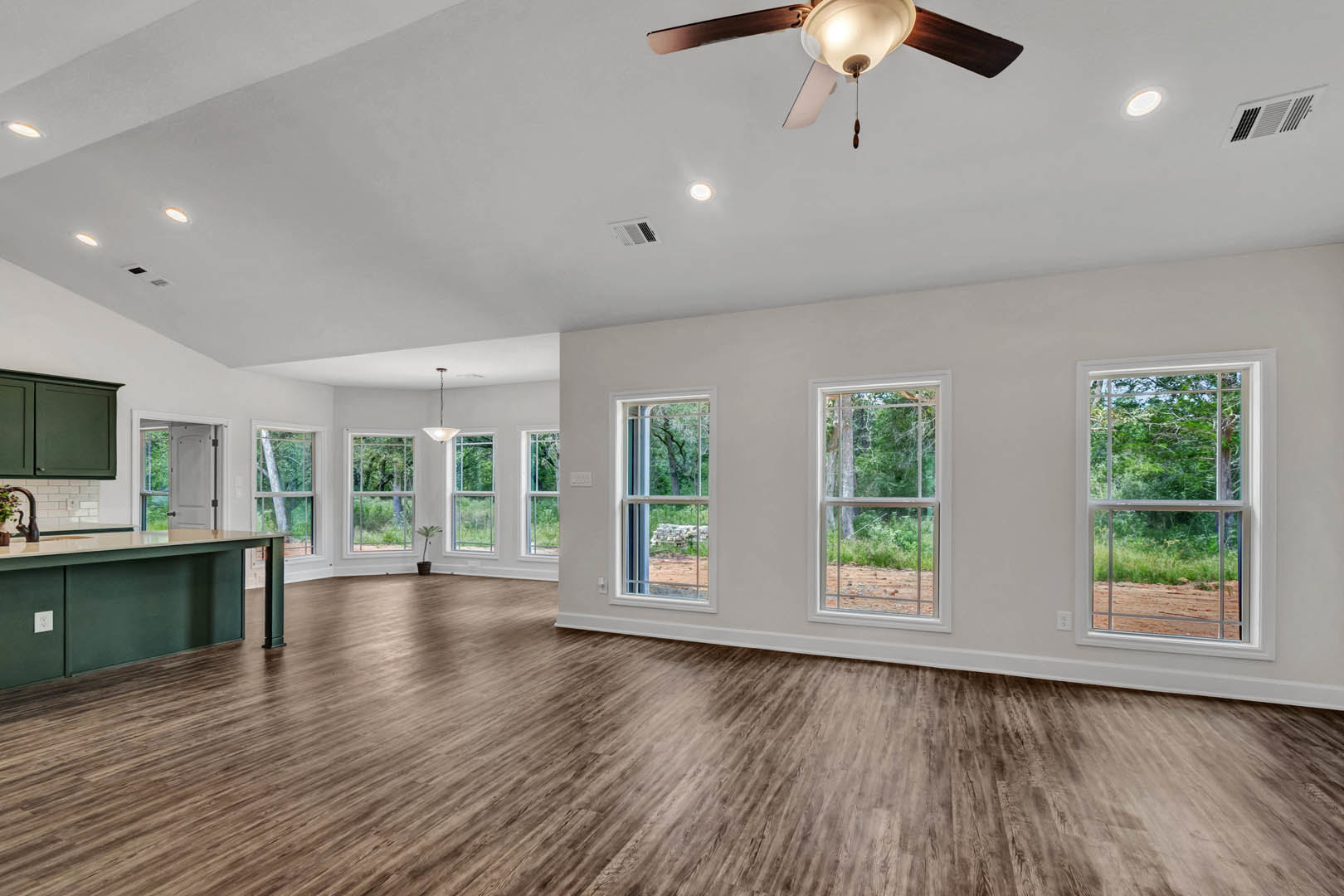 Spacious room with wood flooring, ceiling fan with light, large windows overlooking trees and grassy yard
