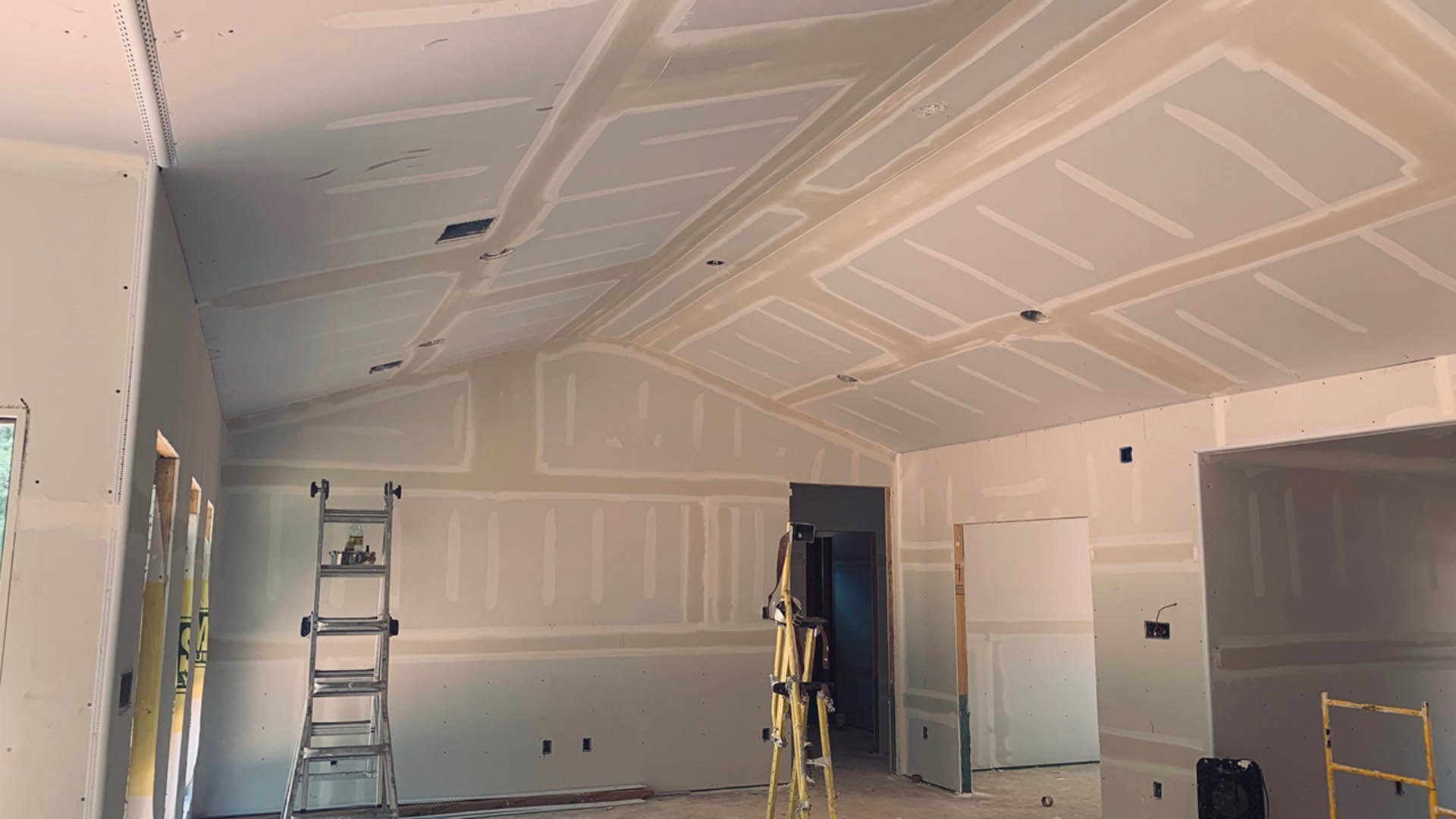 Yellow metal ladder leaning against white plaster wall in a room with exposed ceiling beams and light wood flooring