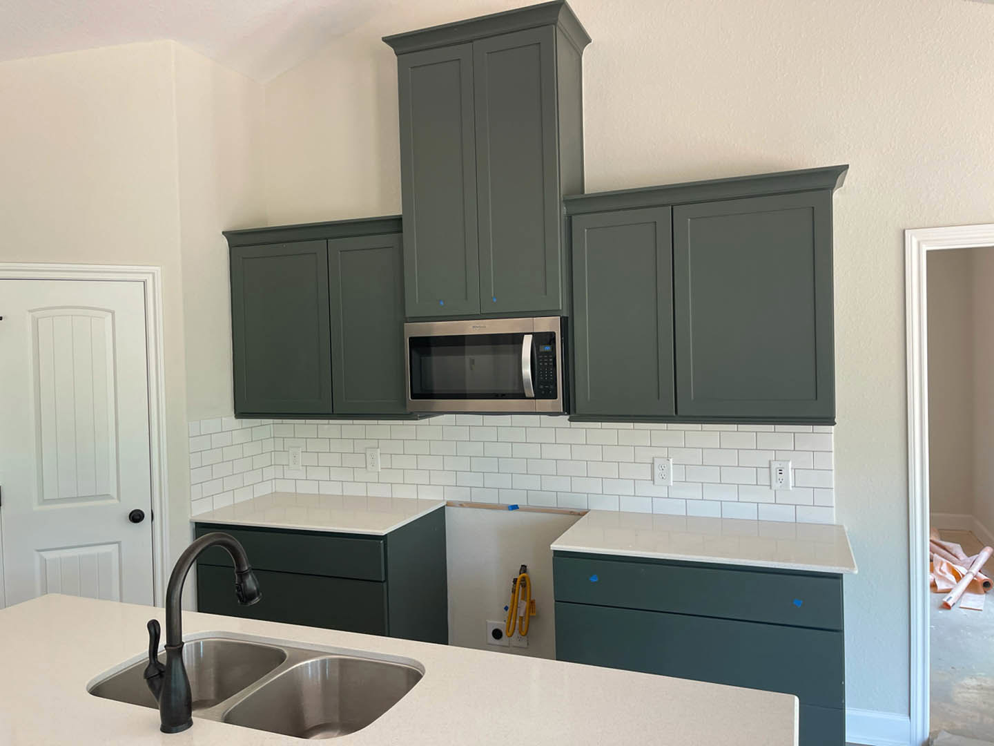 Grey kitchen cabinets and white countertops, open microwave door, stainless steel sink with chrome faucet, yellow hose mounted on wall, close-up of white interior door