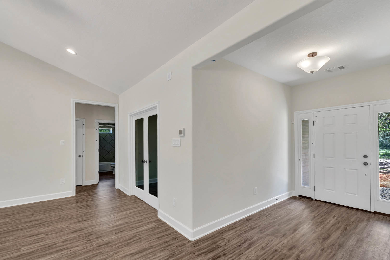 White room with smooth white plaster walls, light wood flooring, white glass-paneled door, and modern ceiling light fixture.