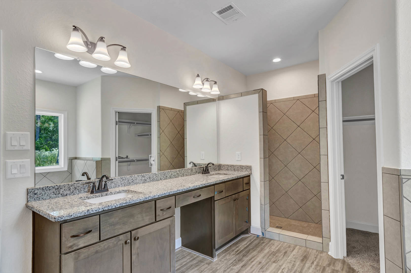 Bathroom featuring marble countertop with undermount sink and drawers, glass-enclosed shower with tile walls, window overlooking forest, modern multi-bulb light fixture, and