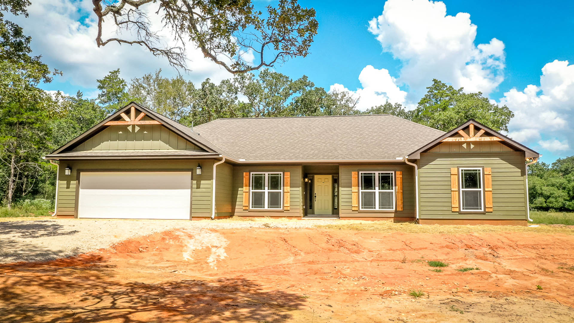 Two-story home with attached garage, concrete driveway, white front door, large windows, and tree branches with green leaves in foreground