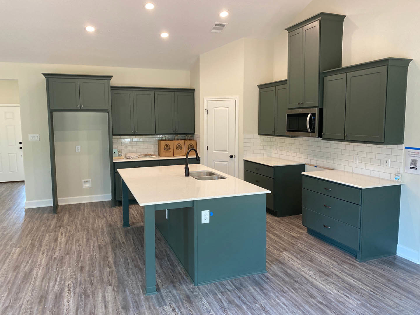 Spacious kitchen featuring a large central island with built-in sink, blue cabinetry with drawers, white walls, tile flooring, and a white door with black handles