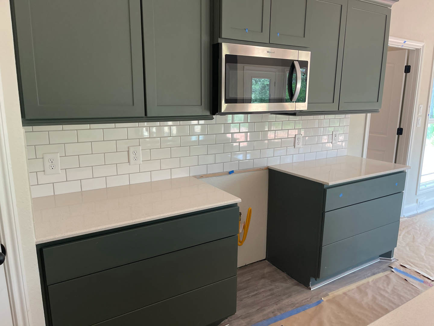 Grey kitchen cabinets with brushed metal hardware, white quartz countertops, built-in microwave, stainless steel sink, and white electrical outlet on tiled backsplash