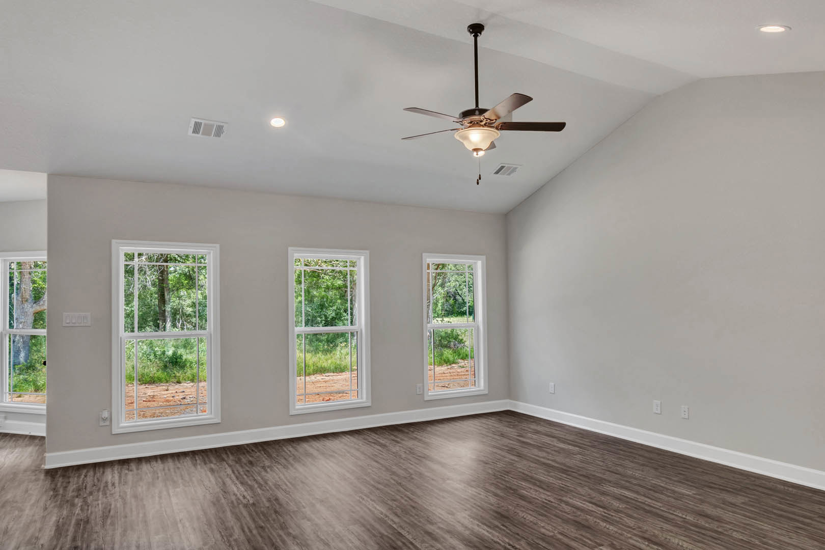 Hardwood floor room with white plaster walls, ceiling fan with light fixture, large windows overlooking green trees and forest