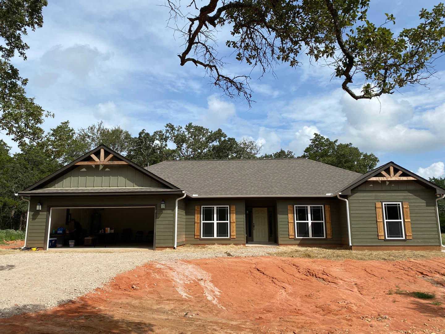 Modern two-story home with attached garage, white siding, black-framed windows, front door, dirt landscaping, and leafy tree branches under blue sky