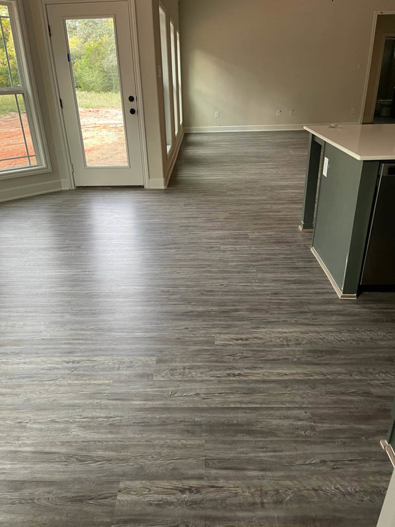 Wood flooring in a modern room featuring a black cabinet, glass door, black accent wall, and window with outdoor view