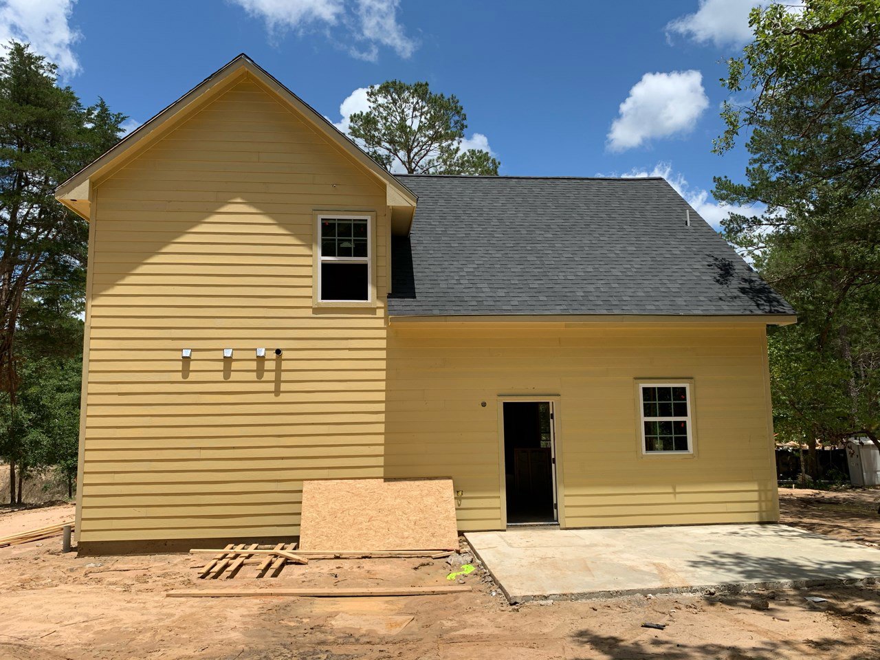 Yellow siding house with black shingle roof, white-framed windows, open front door, and several mailboxes mounted near entry.