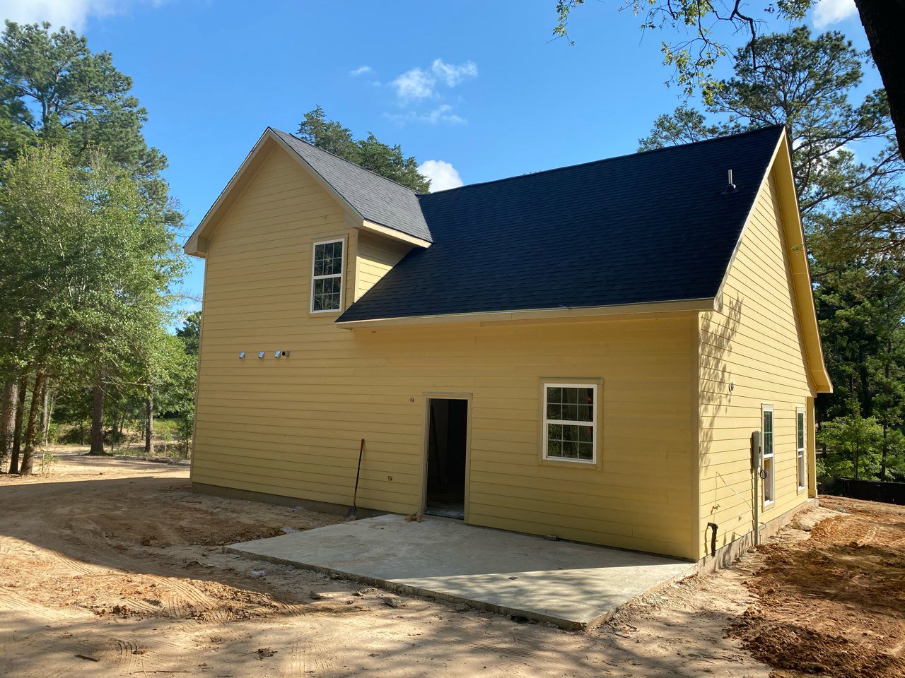 Yellow siding house with black shingle roof, white front door, multi-pane windows with white frames, leafy tree in front yard.