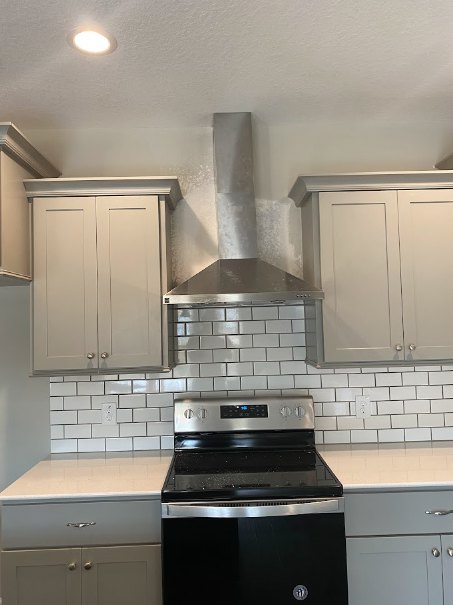 White kitchen cabinets, black and silver stove, light countertops, stainless steel appliances, neutral wall color