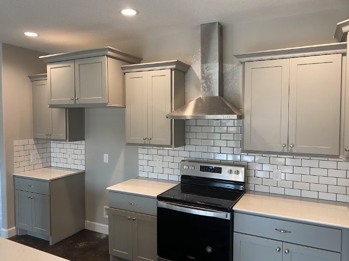 White shaker cabinets, black and silver stove, light quartz countertops, stainless steel range hood, subway tile backsplash