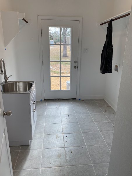 Modern kitchen featuring tile flooring, white cabinetry, stainless steel sink, and a wooden door leading to an adjacent room