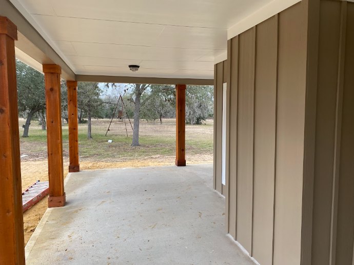 Covered back porch with wooden swing, white trim, glass door, and large windows overlooking landscaped yard