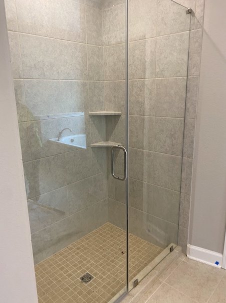 Glass shower enclosure with chrome shower head, white tile walls, and light tile flooring in modern bathroom.