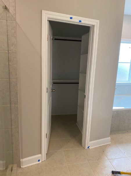 Walk-in closet with built-in white shelves, light wood flooring, plaster walls, and a white door