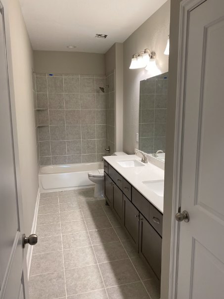 Bathroom with white tile floor, wall-mounted sink and faucet, rectangular mirror above sink, modern toilet, glass-enclosed shower with chrome shower head, neutral wall tiles