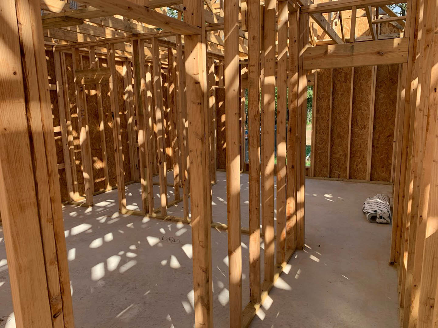 Wooden house frame with exposed beams and lumber, set outdoors on bare ground
