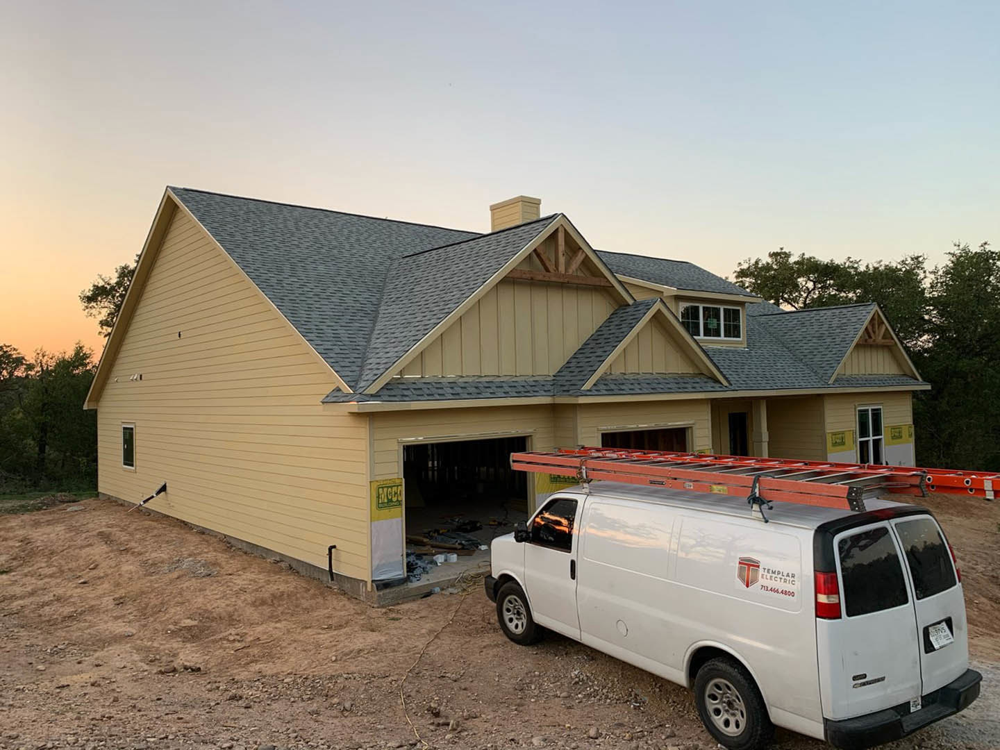 White van with roof ladder parked in driveway in front of modern house with light siding, large windows, and tree-lined yard