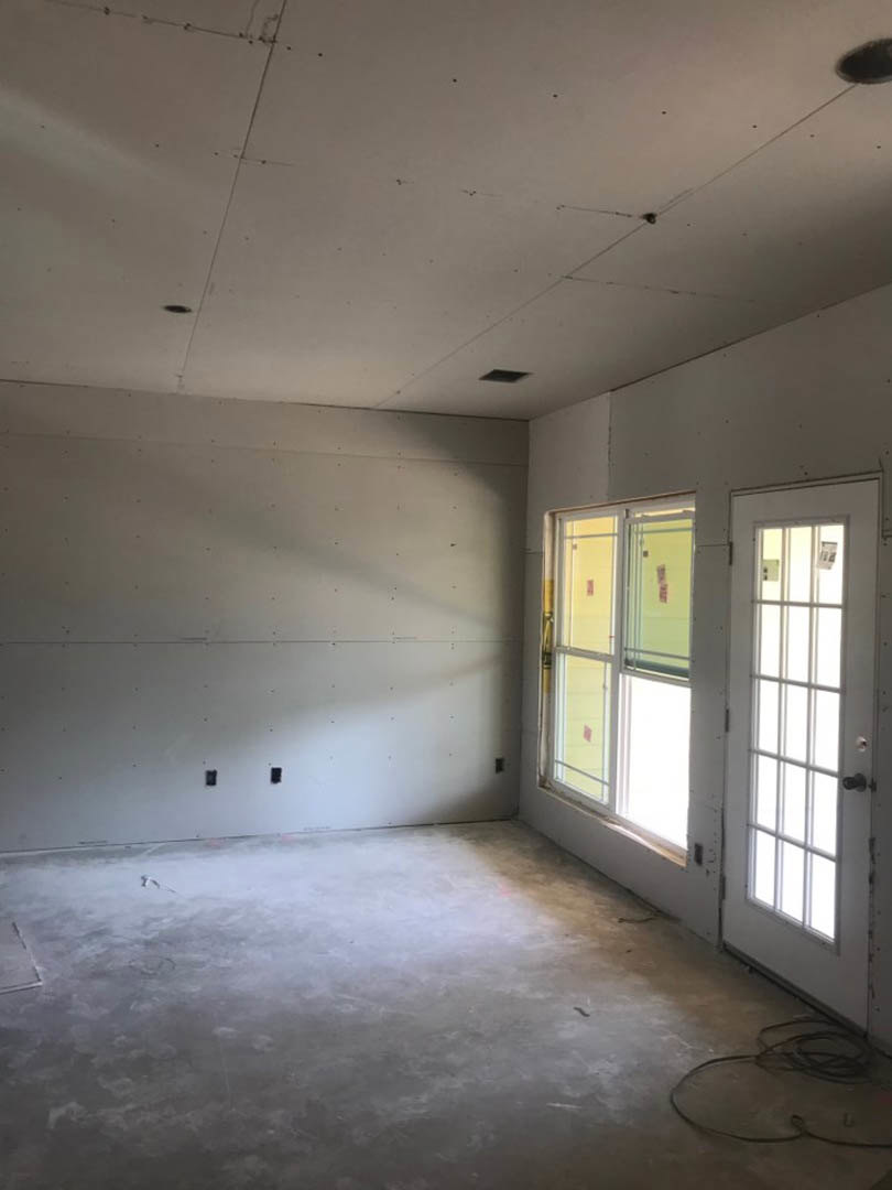 Concrete floor with black wire, white plaster walls, white door with glass panes, large window allowing daylight into unfinished room