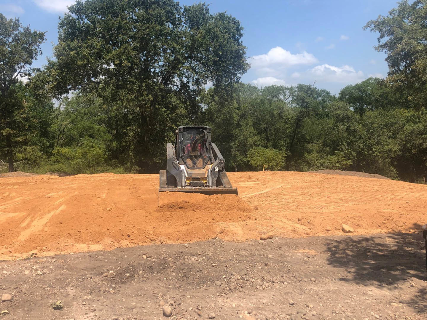 Yellow bulldozer with large tires parked on a dirt clearing near tall trees under a blue sky
