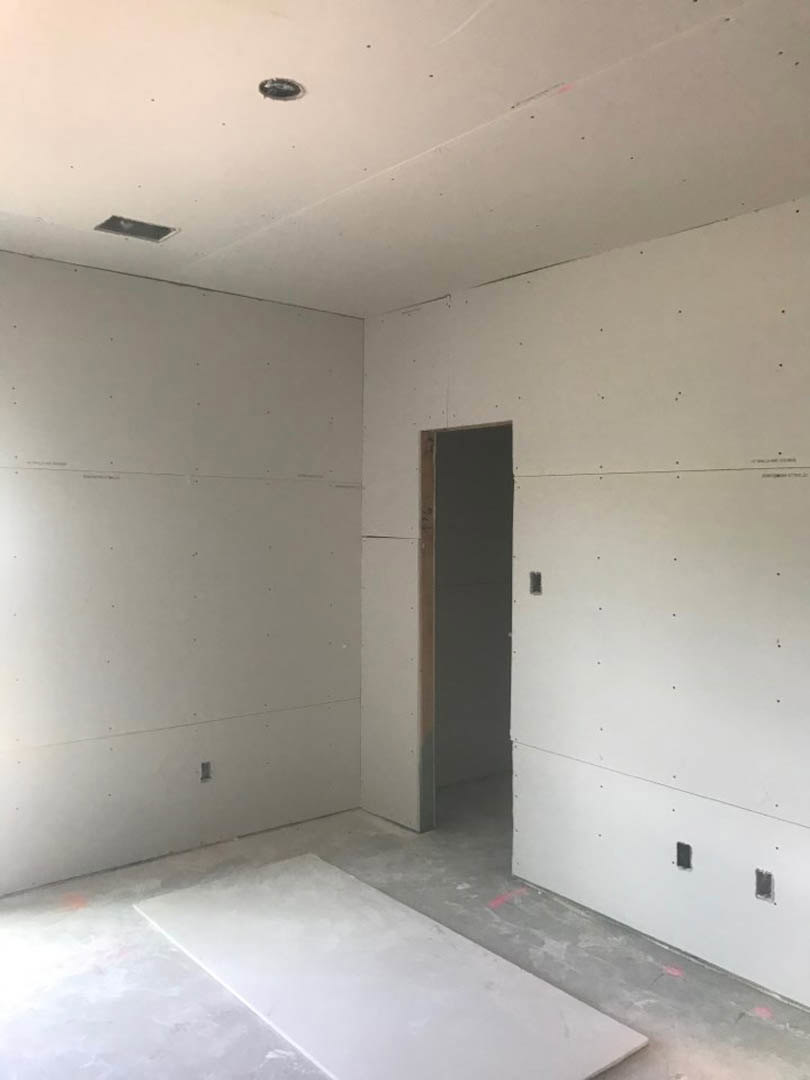 White plaster wall with small holes, open white door, concrete floor, and ceiling in a modern interior room