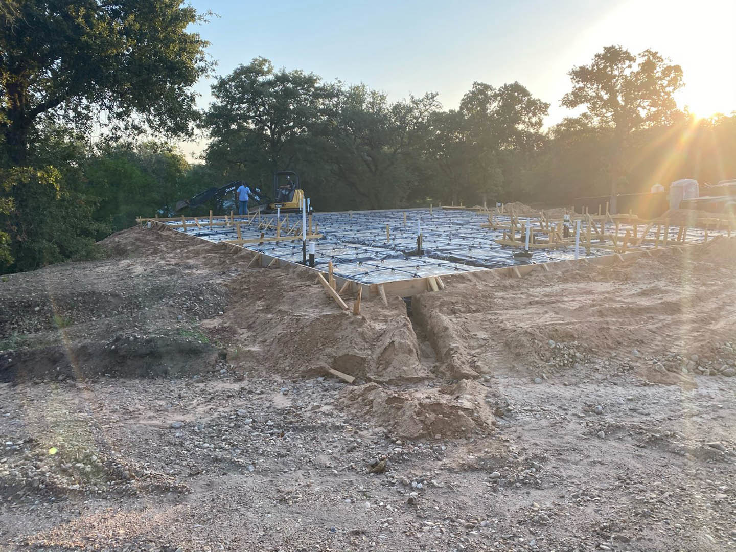 Bulldozer clearing dirt on residential construction site, surrounded by tall trees and sunlight filtering through foliage
