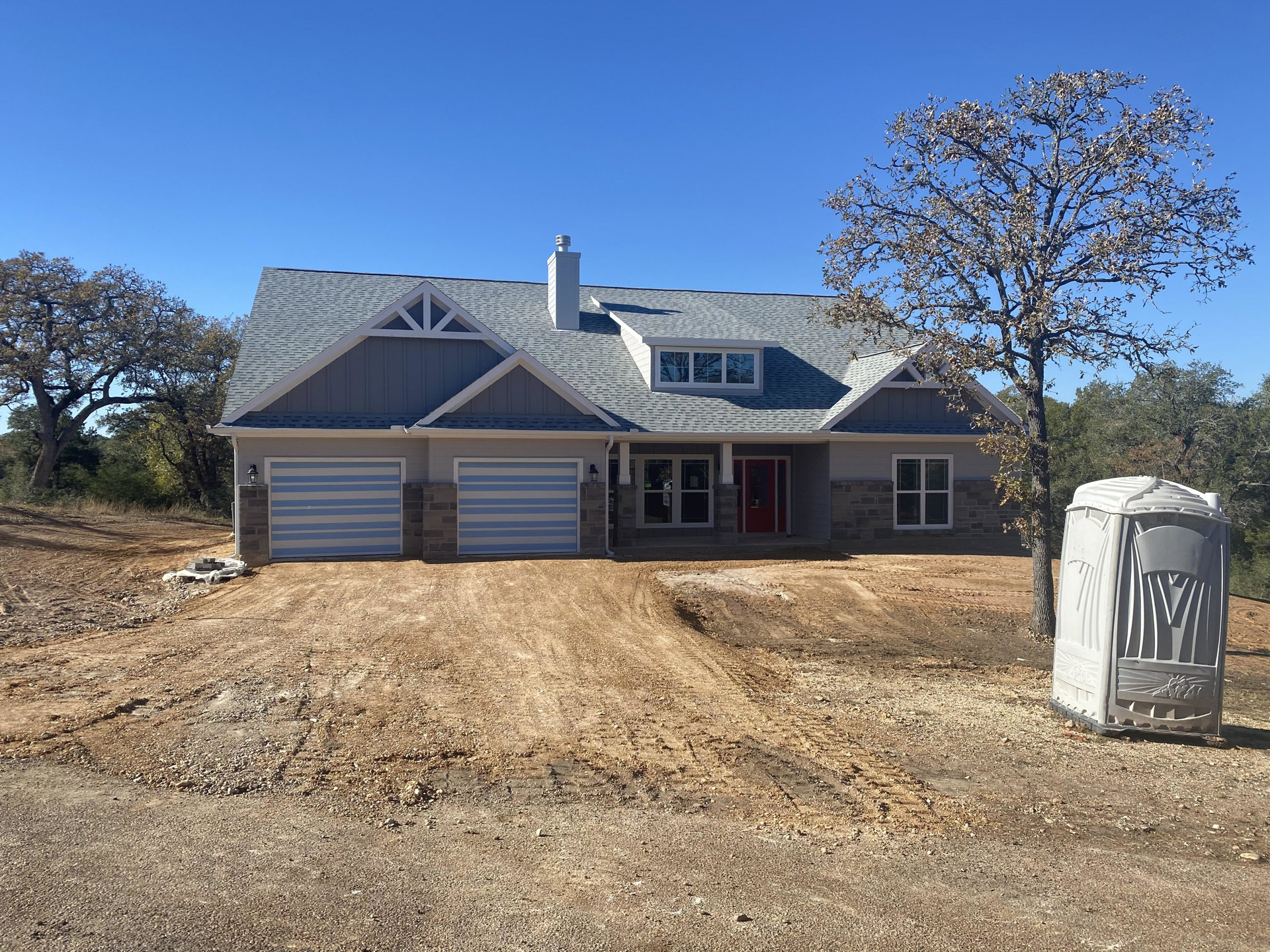 Two-story home with light siding, attached garage, red front door, paved driveway, and mature tree in front yard