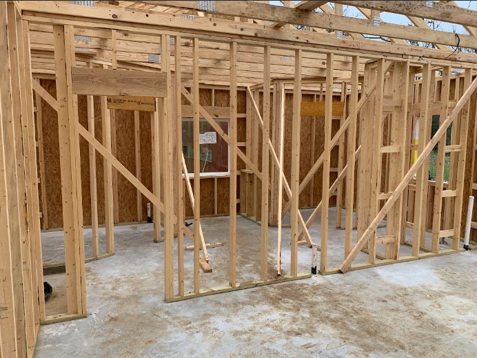Exposed wooden beams and framing with construction insulation, unfinished interior, window featuring a sign