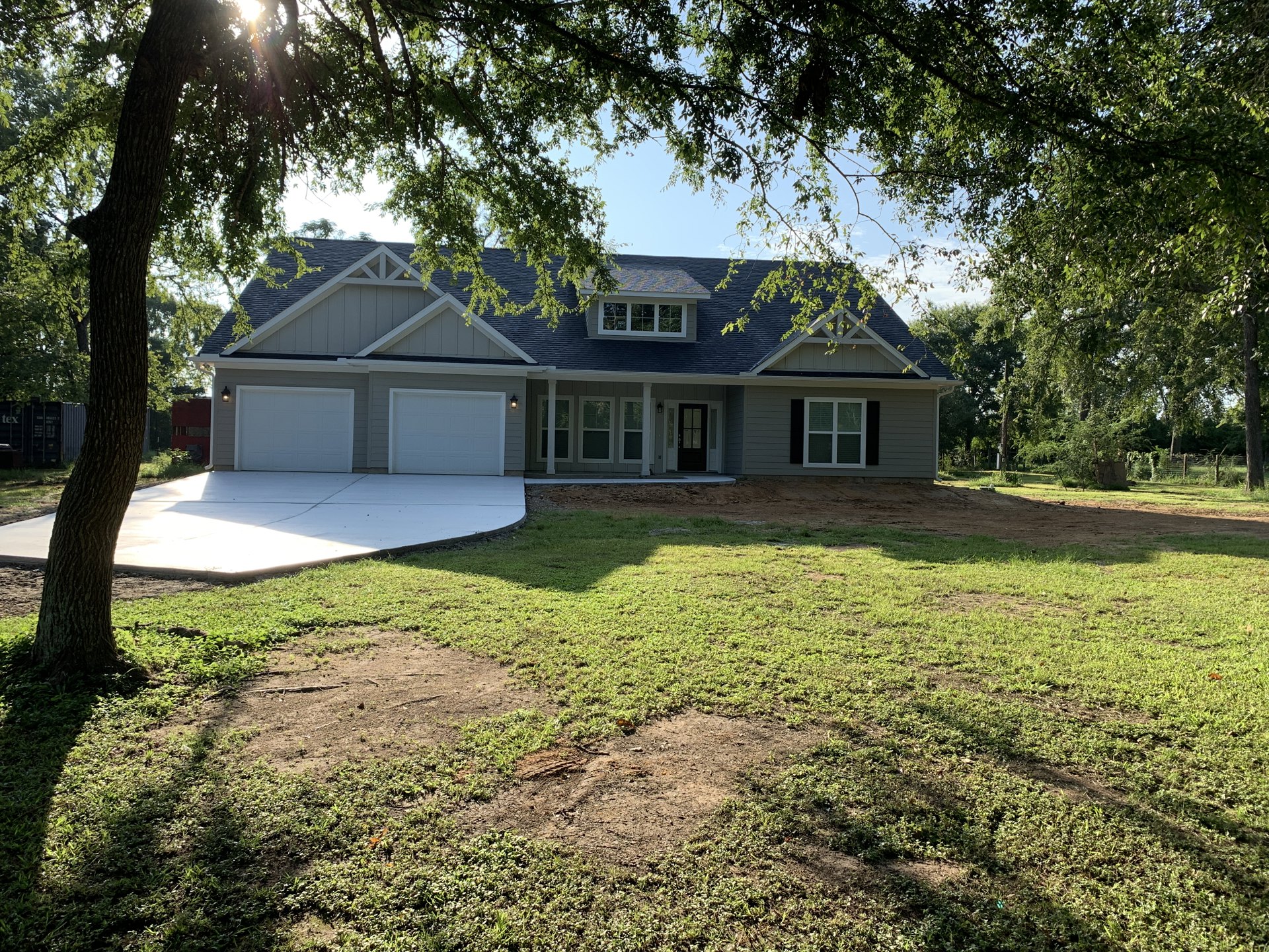 Two-story house with white garage door, concrete driveway, green lawn, mature tree, and windows with white blinds