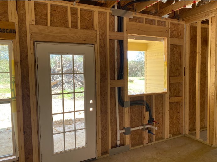 Wood-framed door and window with hardwood beams and planks, metal sign mounted on adjacent wall, interior view of custom home.