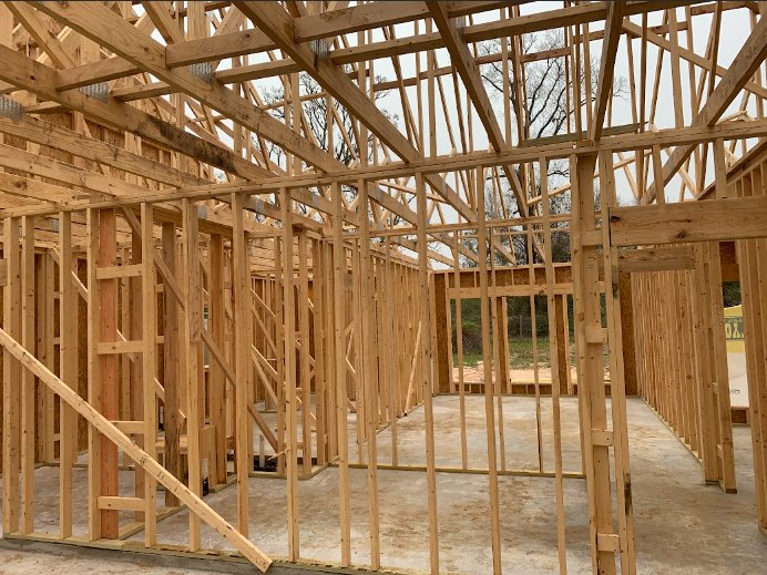 Exposed wooden beams and planks forming the structural frame of a house under construction, with unfinished lumber and open interior spaces visible