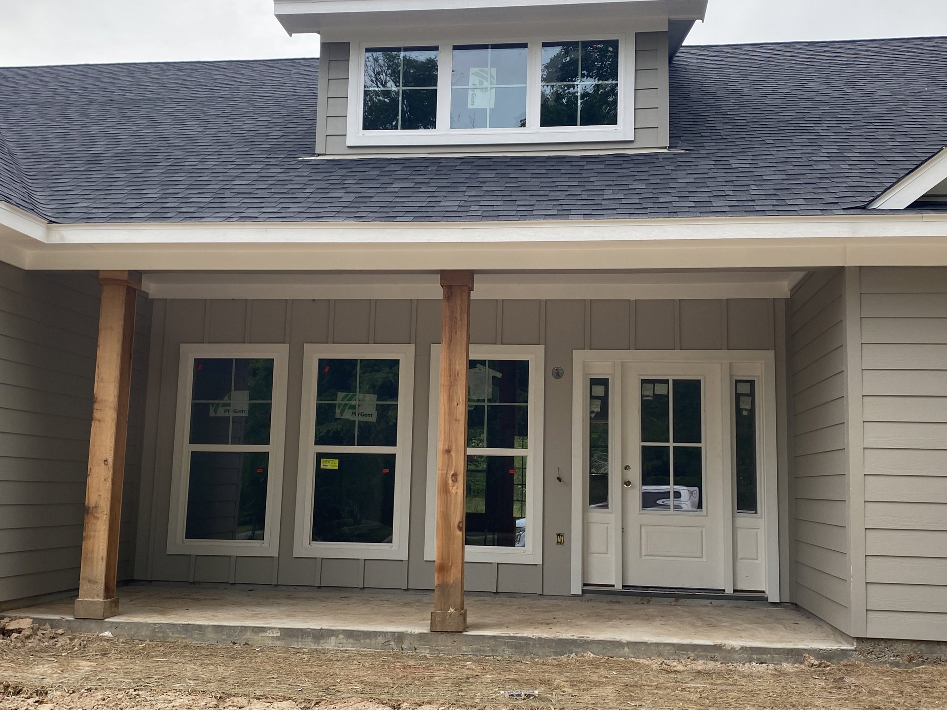 Front porch with wooden posts, white door with glass panels, sash window displaying a sign, horizontal siding, exposed wood beam with visible knot