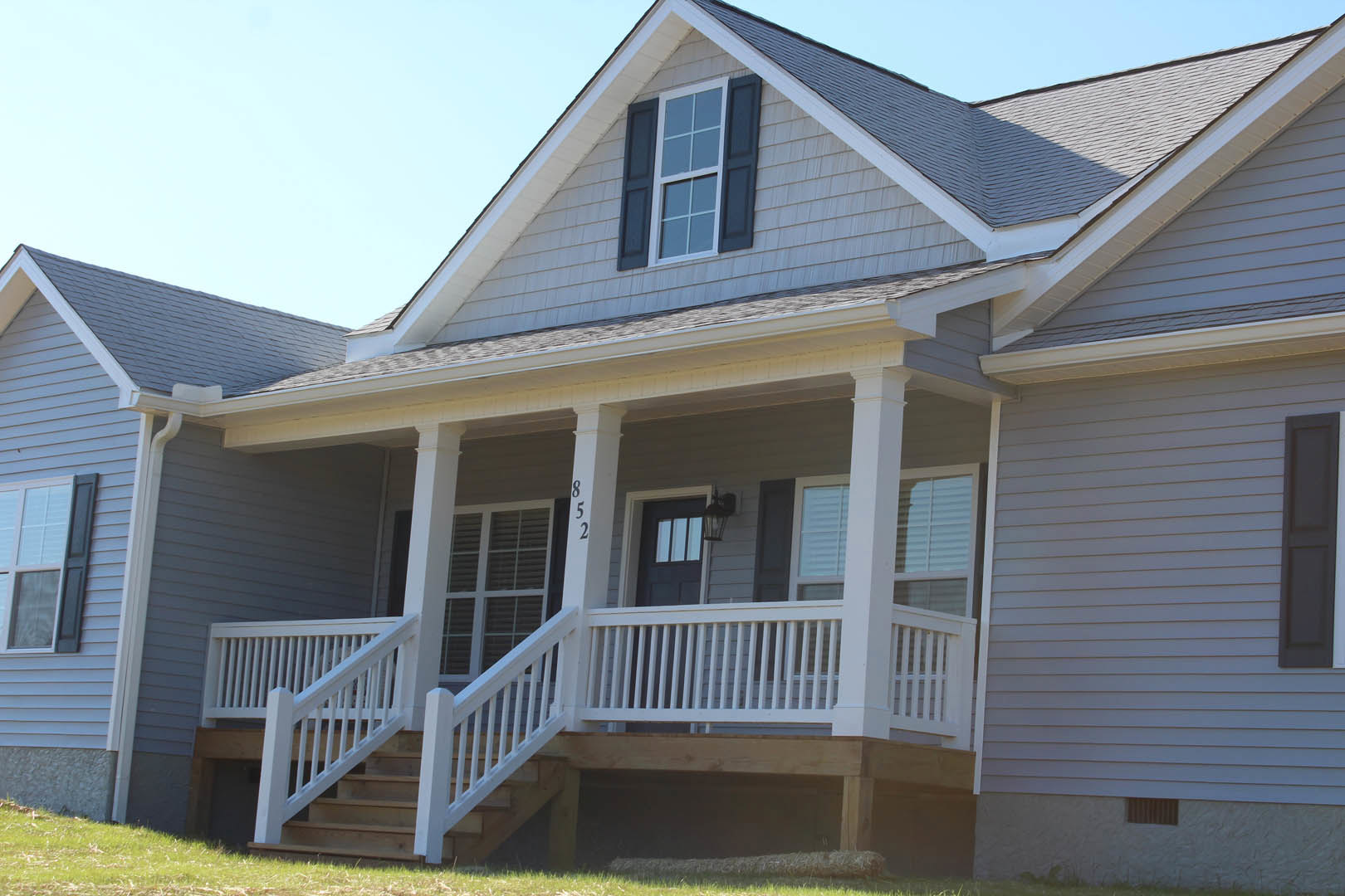 Two-story home with light-colored siding, white porch railing, front stairs, and sash windows with white frames