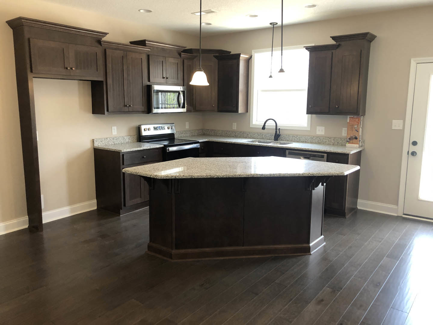 Spacious kitchen featuring a large marble-topped island, black curved faucet, tile backsplash, stainless steel microwave, stove, and white cabinetry