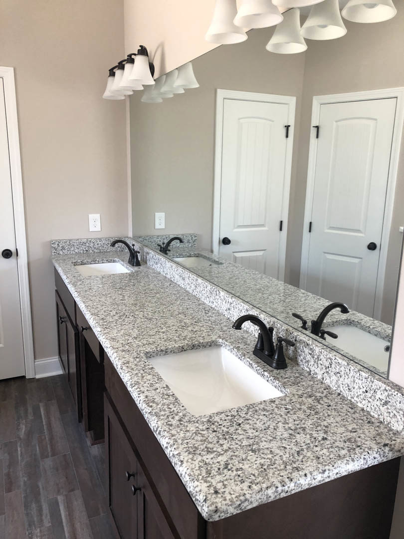 Bathroom with two white square sinks set in a black speckled granite countertop, large wall mirror above, white cabinetry below, and a white door with black hardware visible in the