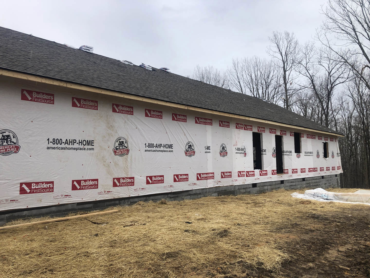 Modern house exterior with white siding, red and white signs attached to the wall, grassy yard in foreground, and trees under a partly cloudy sky