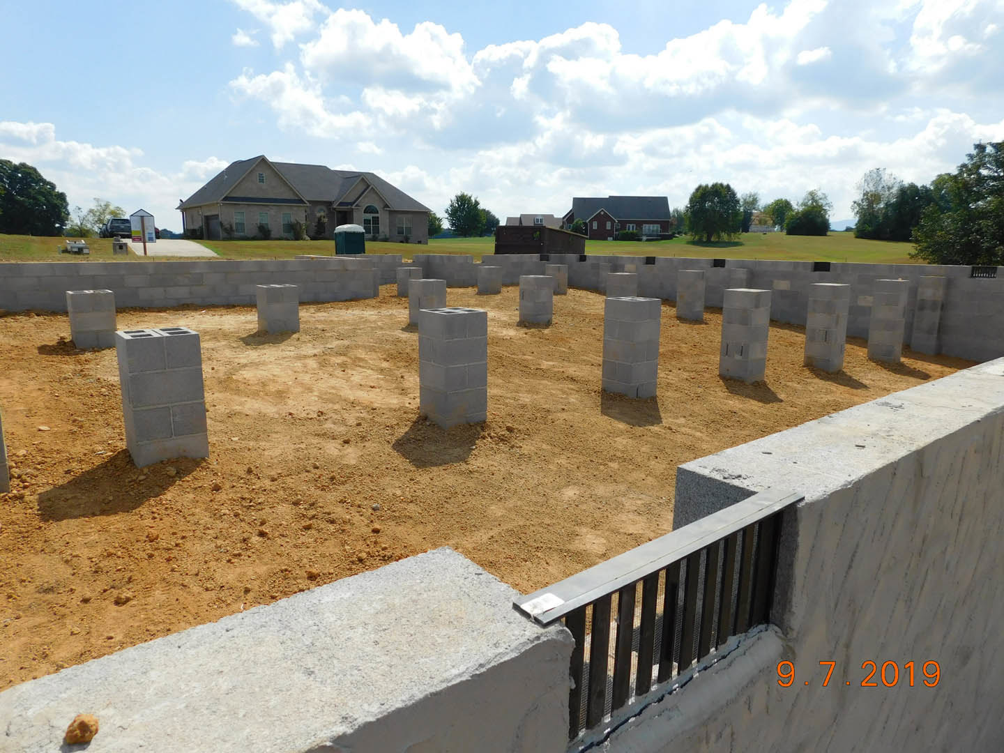 Construction site with stacked concrete blocks arranged in a circle on grassy land, surrounded by trees and cloudy sky