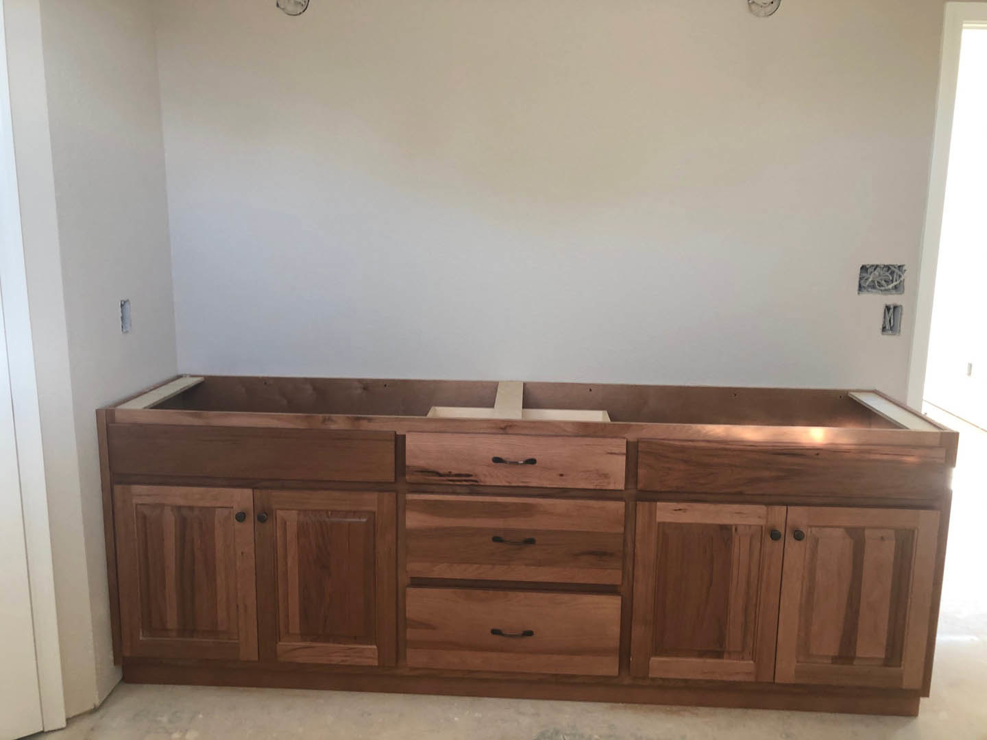 Light wood kitchen cabinets with drawers, white countertop featuring an undermount sink and chrome faucet, white wall backdrop, hardwood flooring