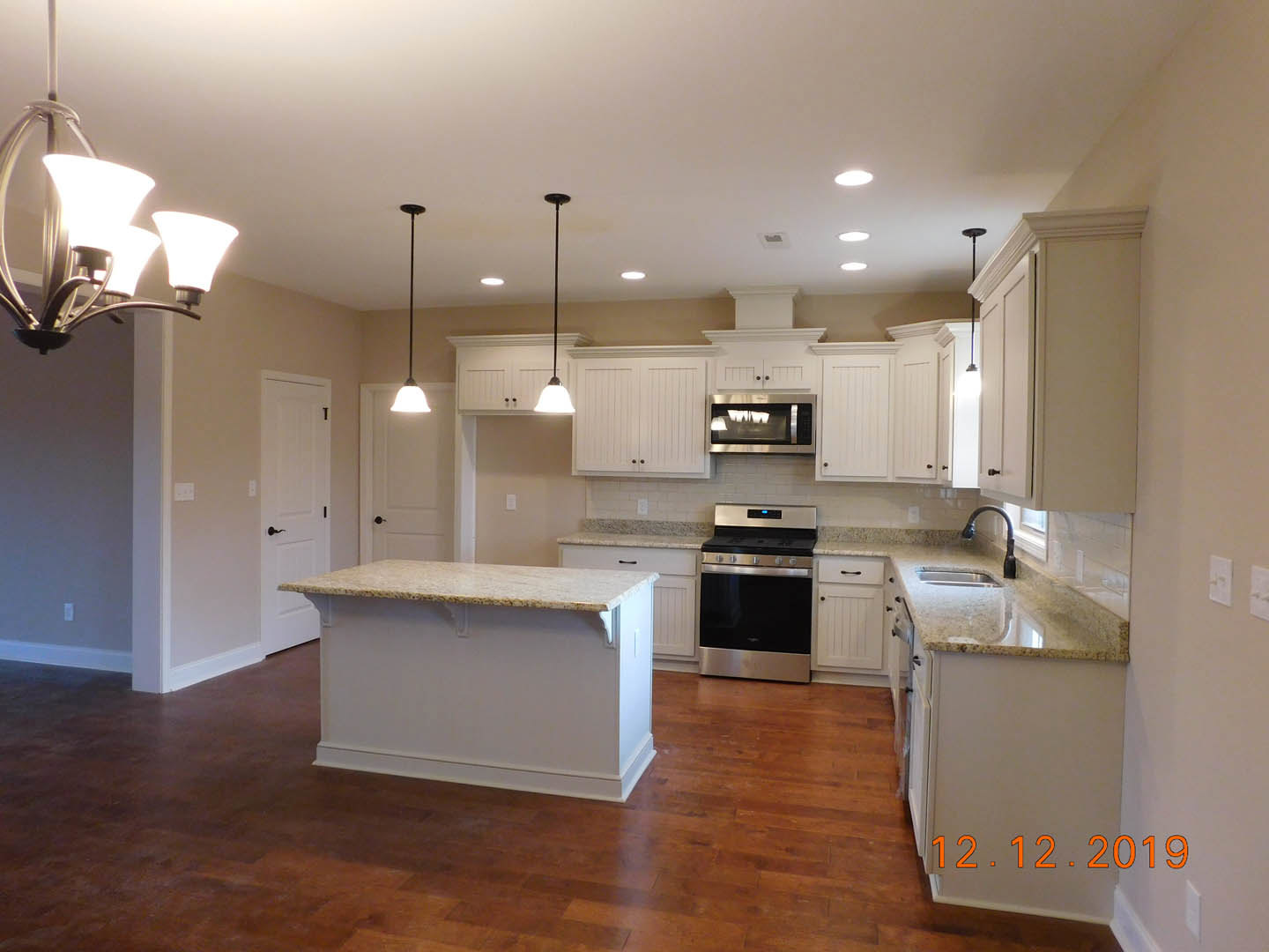 White shaker cabinets, marble countertops, stainless steel stove and microwave, wood plank flooring, modern chandelier, neutral walls