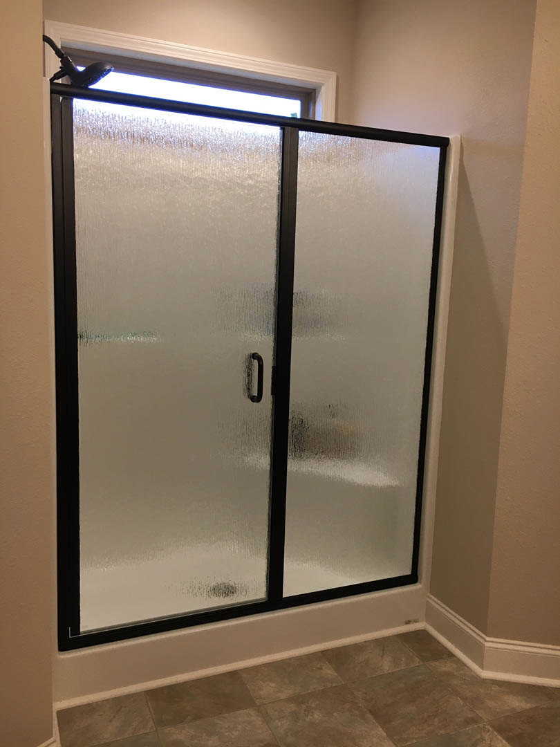 Shower enclosure with frosted glass doors and black metal frame, tile floor, stone accent, and visible plumbing fixture