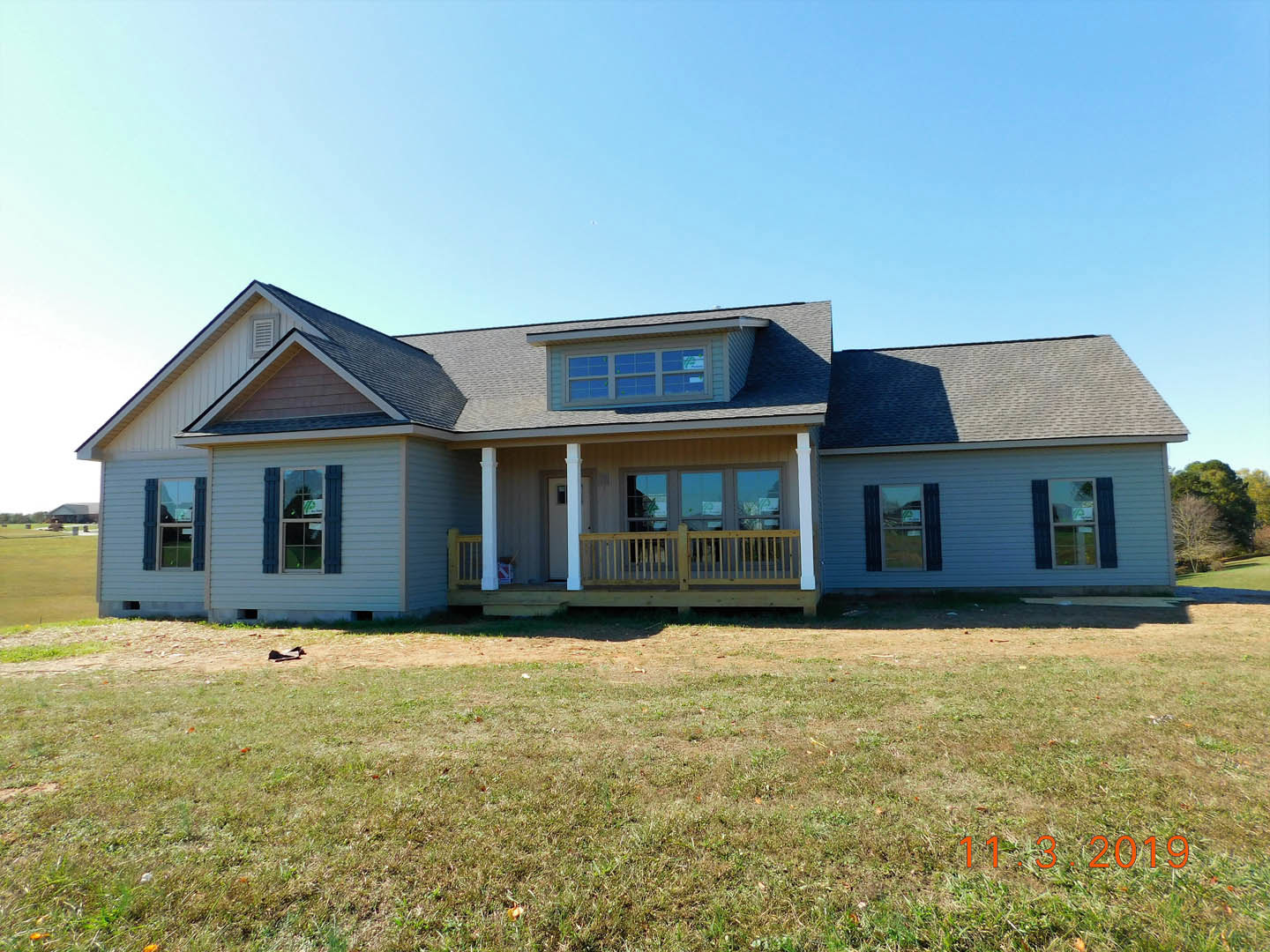 Two-story house with covered porch, upper balcony, large windows, manicured lawn, wooden railing, and clear blue sky