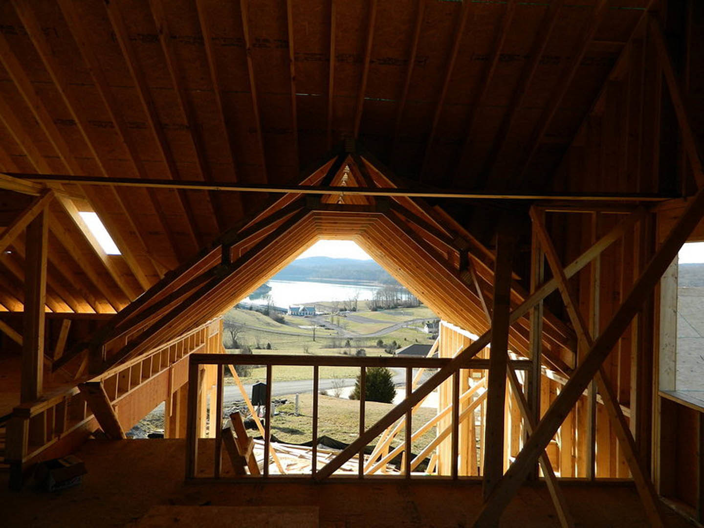 Wooden ceiling with exposed triangular beam, large window framing lake view, tree visible outside, warm light glowing from interior window.