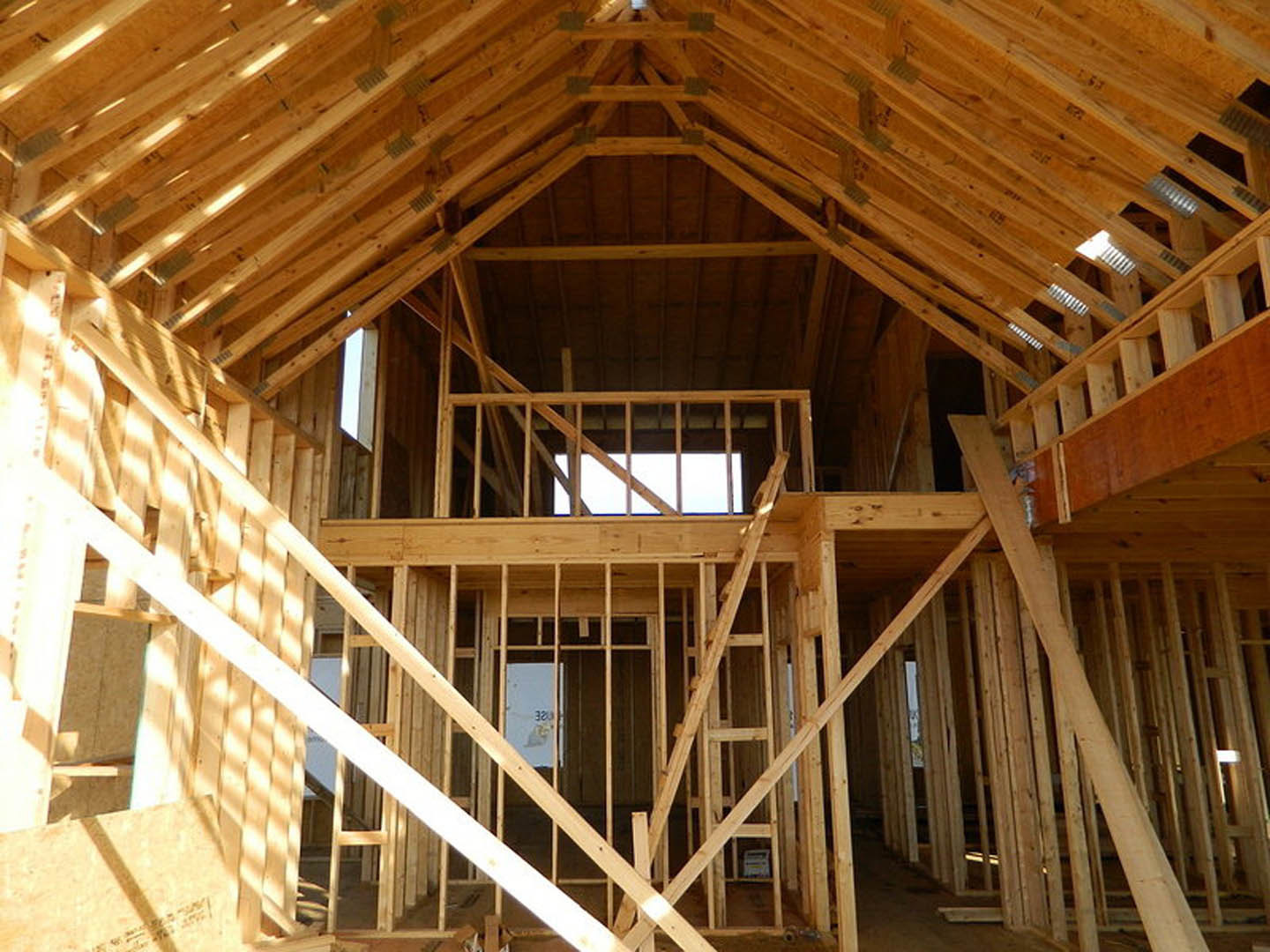 Exposed wooden beams and framing in a partially constructed attic with visible ceiling planks and insulation