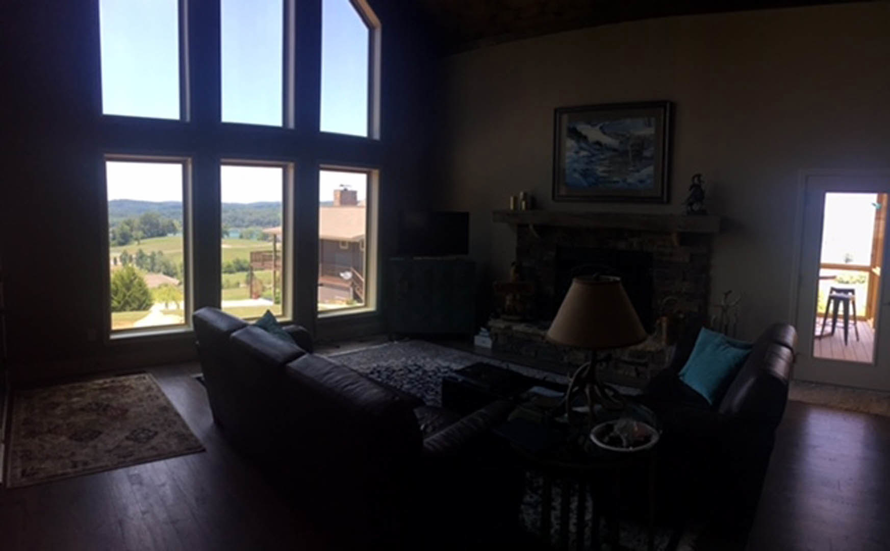 Living room with stone fireplace, gray upholstered couch, wood floors, large windows, and decorative pillows
