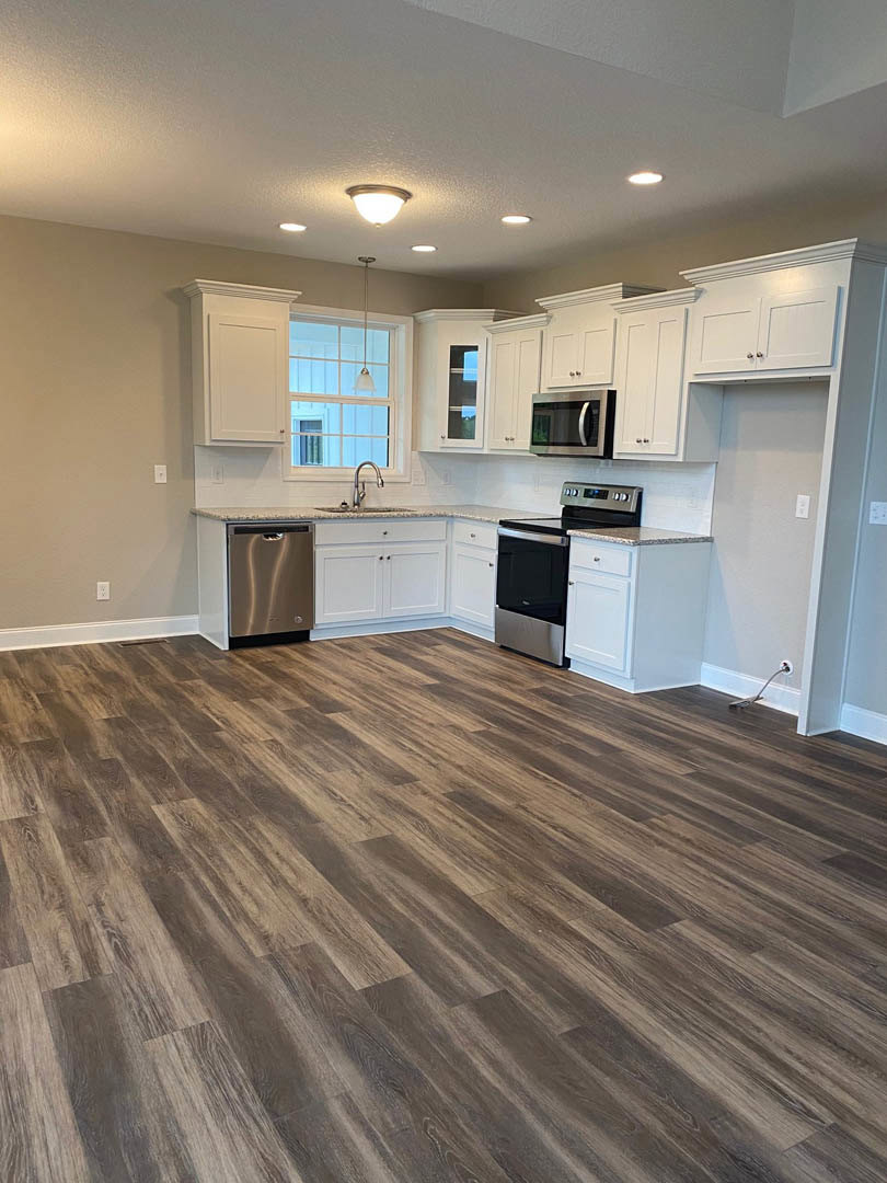 White kitchen cabinets, stainless steel appliances including microwave, dishwasher, and stove, wood flooring, light fixture on ceiling, neutral walls, stone countertop