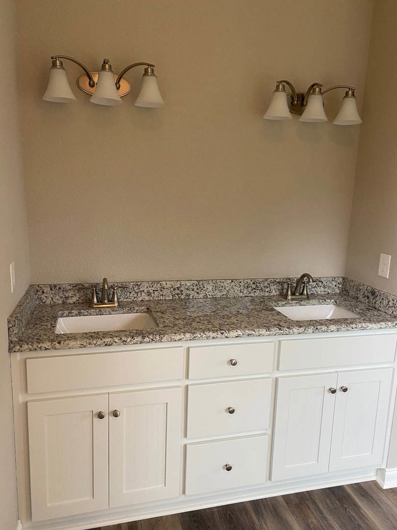 Bathroom with marble countertops, white cabinets, black-bordered white walls, black speckled surface, chrome faucet, and drawers beneath the sink.