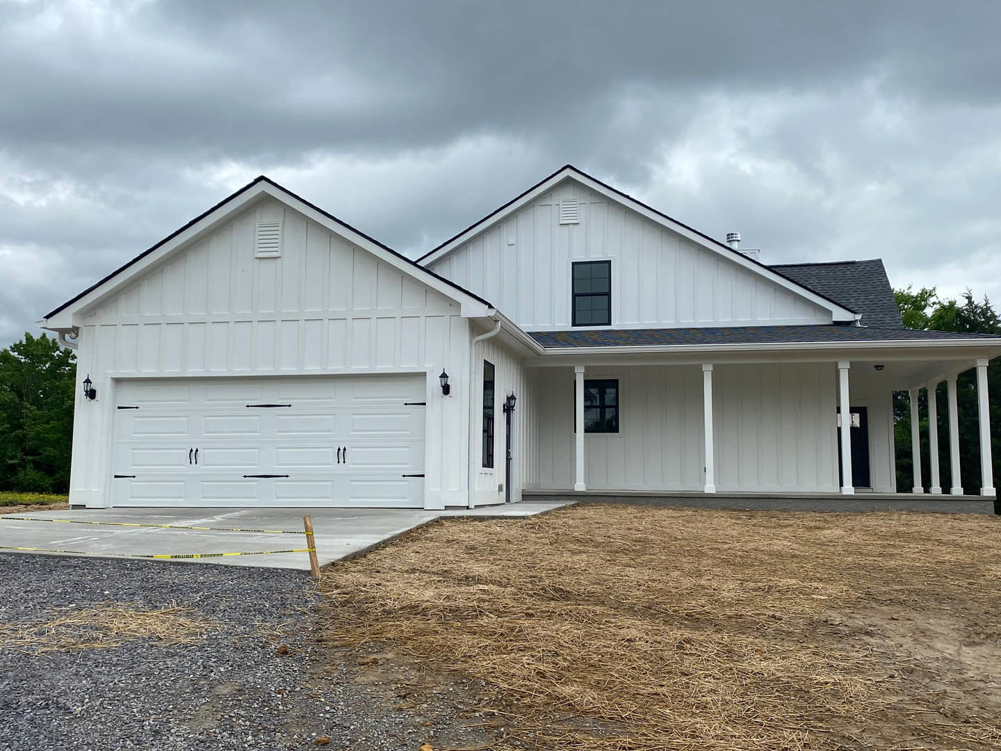 White house with black-framed windows, attached garage, concrete driveway, cloudy grey sky, and American Gothic House visible in the background